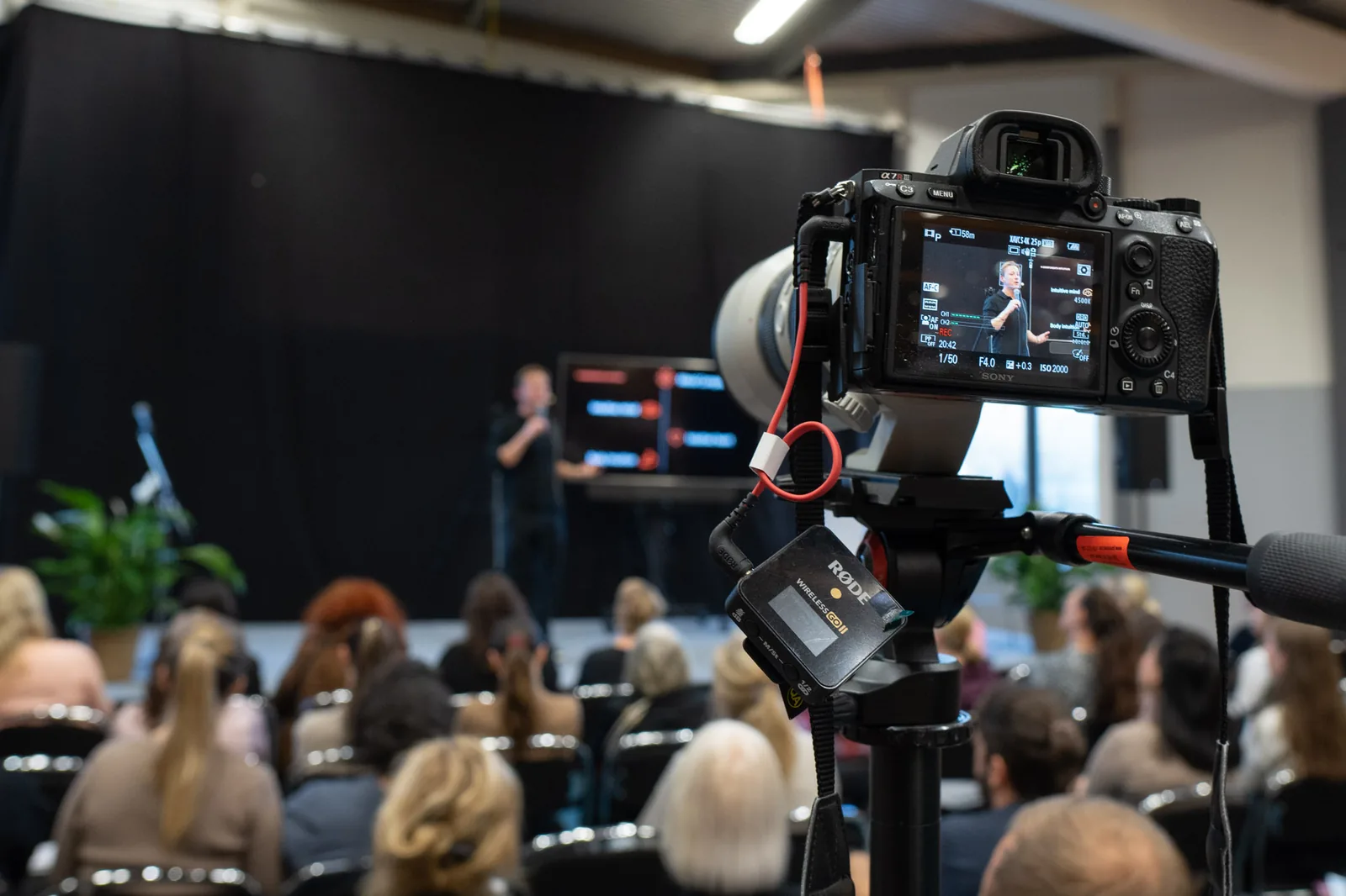 Maurice Jenkens speaking on stage, filmed at a live event